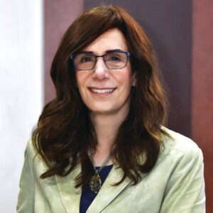 “Judy Faulkner, founder and CEO of Epic Systems, sitting in her Madison, Wisconsin office with a computer and books, symbolizing her healthcare empire.”